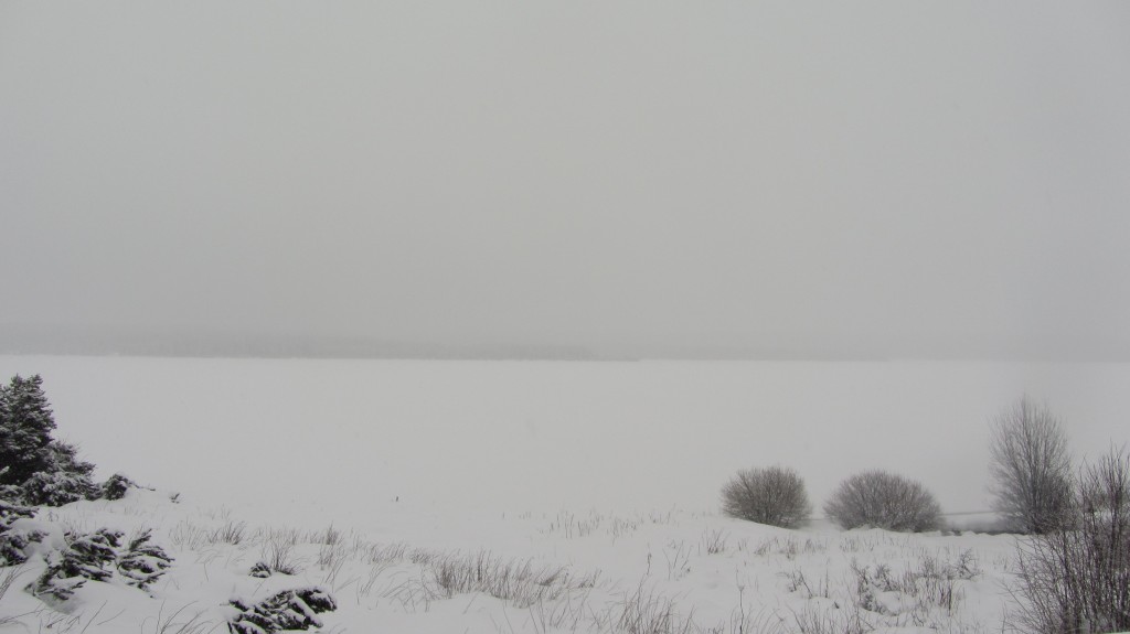 Le lac couvert de glace au mois de janvier. Entre la neige et le brouillard, la ligne d'horizon est confuse.